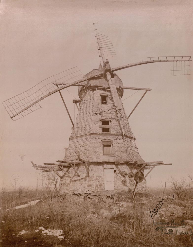 Photograph of the Lawrence Windmill with a man sitting where the arms of the windmill intersect