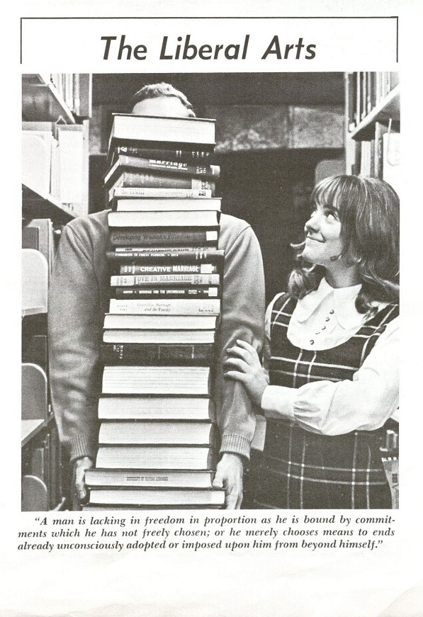 Photograph of a female KU student with the object of her affection behind a stack of books, 1970