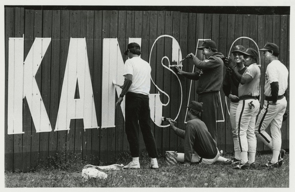 Photograph of the baseball team painting "KANSAS" on a fence, 1984-1985