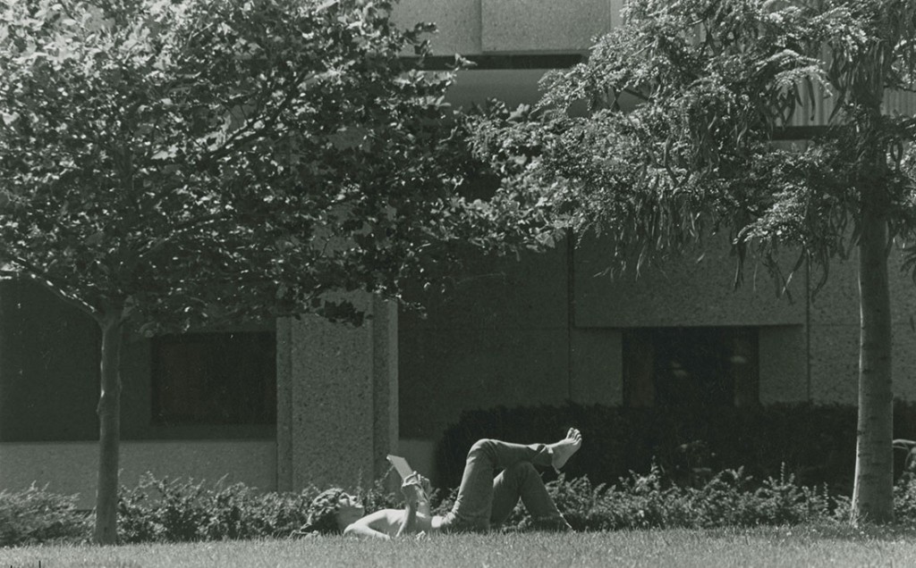 Photograph of a student reading in the grass in front of Wescoe Hall, 1981