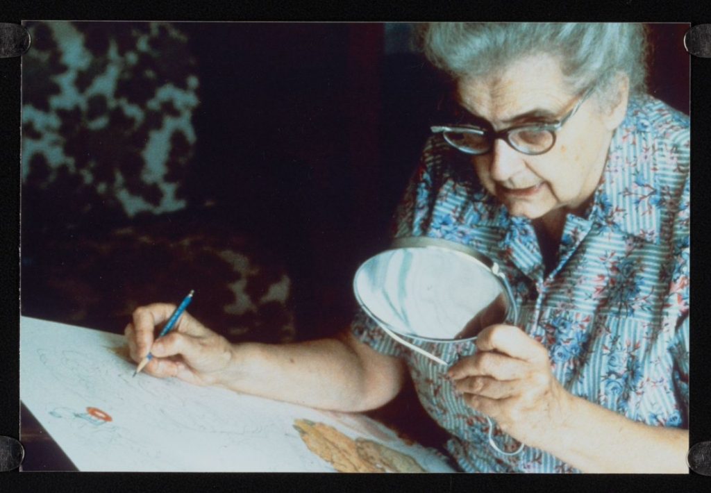 Close-up color photograph of an older woman drawing in one hand and holding up a mirror to her face in the other.
