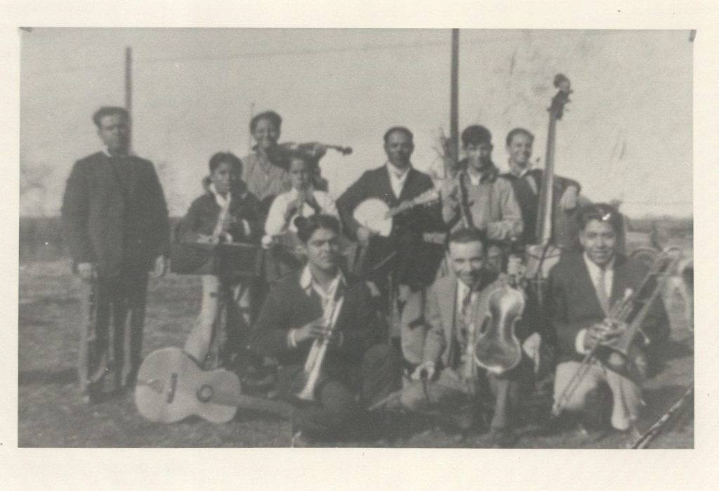 Black-and-white photo of individuals - mostly if not entirely men - outside with their instruments.
