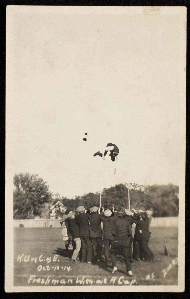 Photograph of a group of men tossing a freshman caught without his cap, 1914