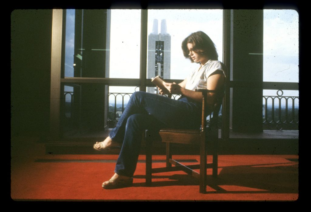 Photograph of a library student assistant reading a book in the North Gallery at Spencer Research Library, 1970s 