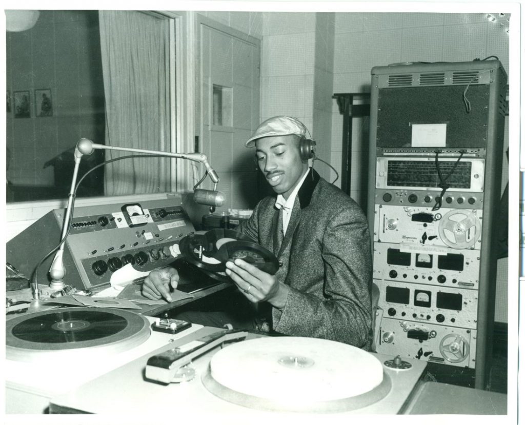 Photograph of Wilt Chamberlain looking at vinyl records in a radio studio, 1955-1958