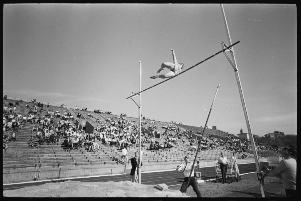 Photograph of an athlete at mid-height of a pole vault, 1965