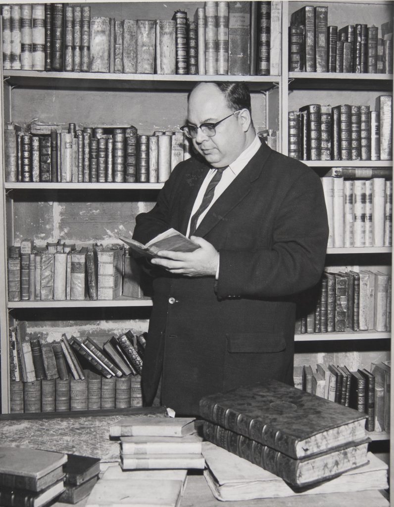 Man holding book, in front of bookshelf