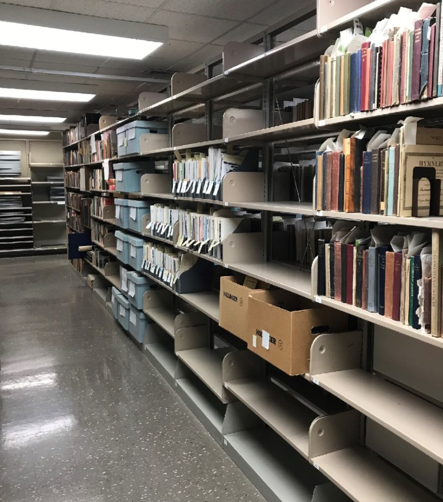 A row of book shelves; many have books or archival boxes on them.