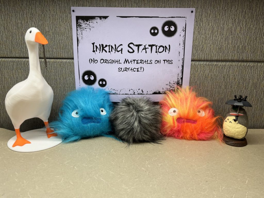 Five small items in front of a sign that reads "Inking Station; No Original Materials on This Surface!"