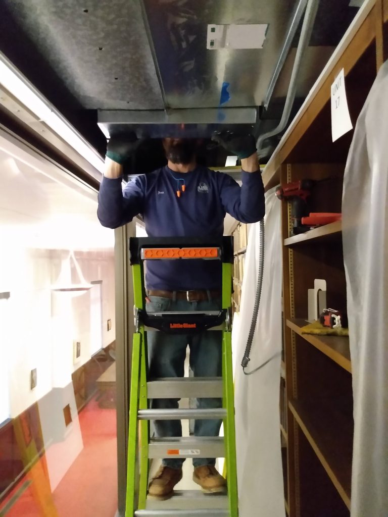 HVAC installer on ladder, with head in the ceiling ductwork.