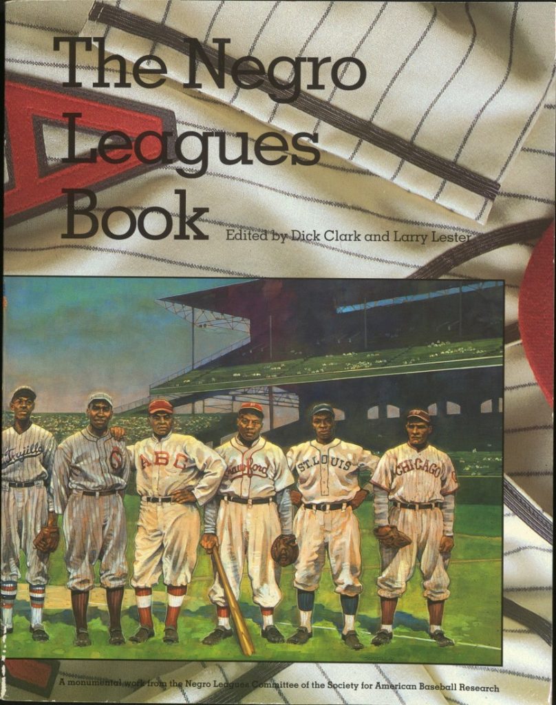 Color illustration of Negro League players standing in a baseball stadium. The cover's background is part of a uniform.