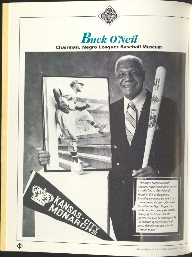 Black-and-white photograph of Buck O'Neil standing with a baseball bat on his left shoulder. He is also holding a photograph of himself as a young baseball player. There is a Monarchs pennant and a message from O'Neil.