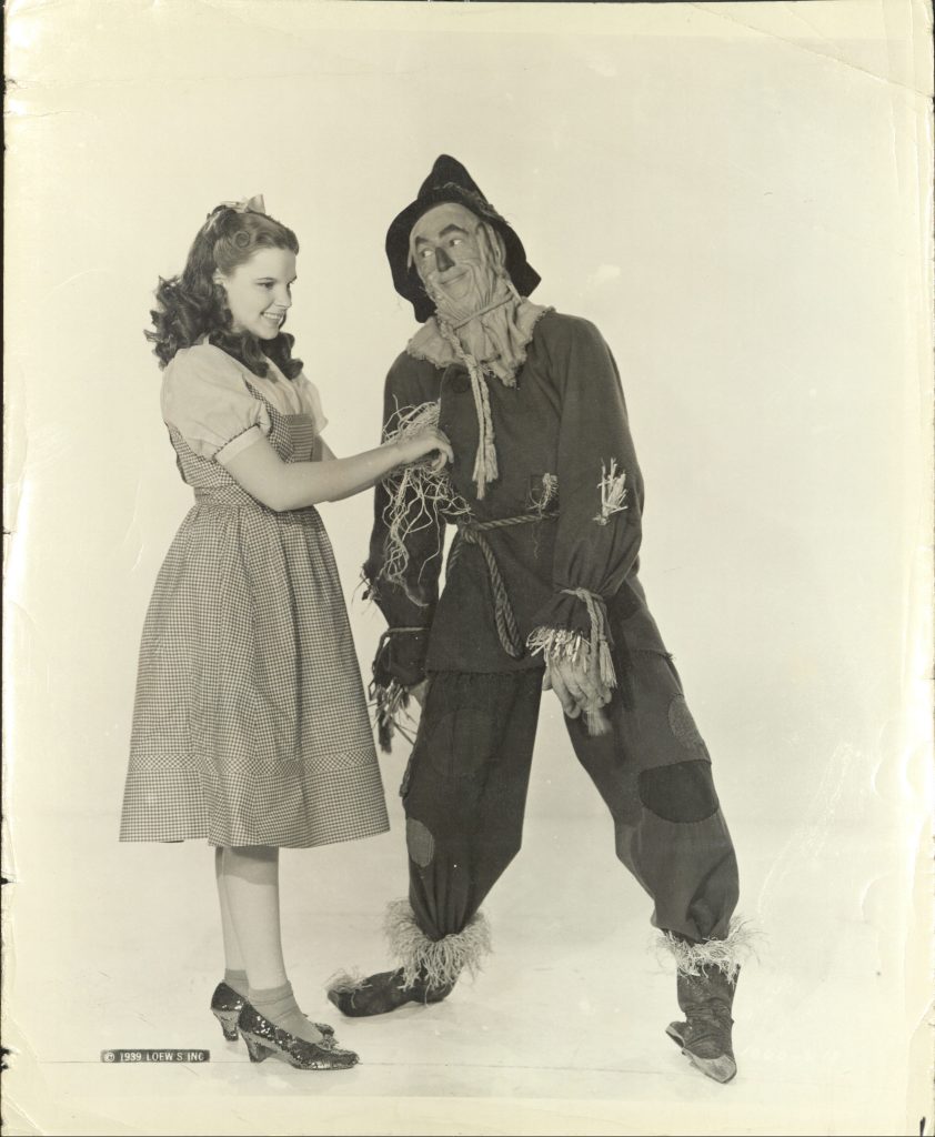 A young girl in a dress replacing the straw stuffing of the scarecrow.