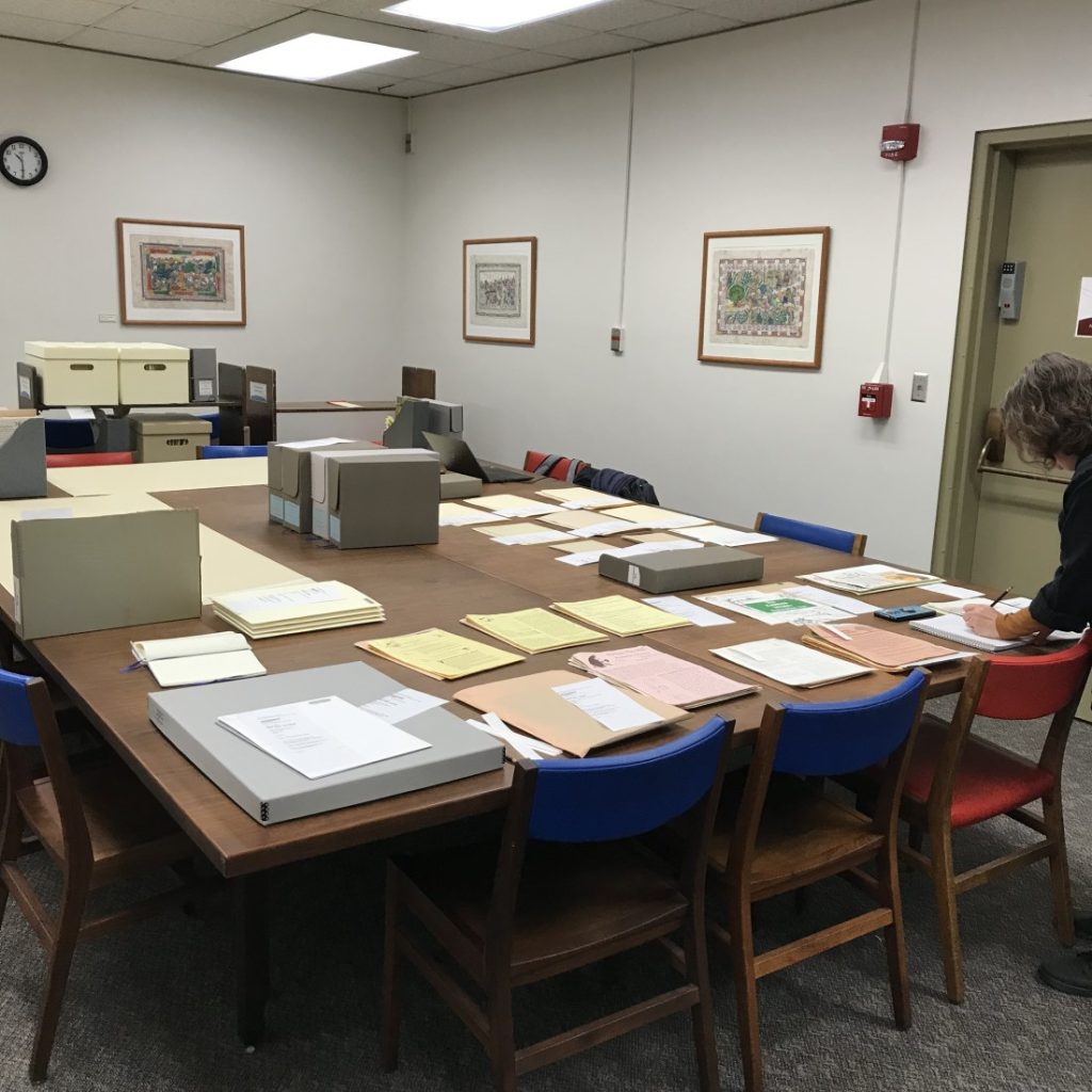 Archival boxes, folders, and documents covering a large table in a library classroom.