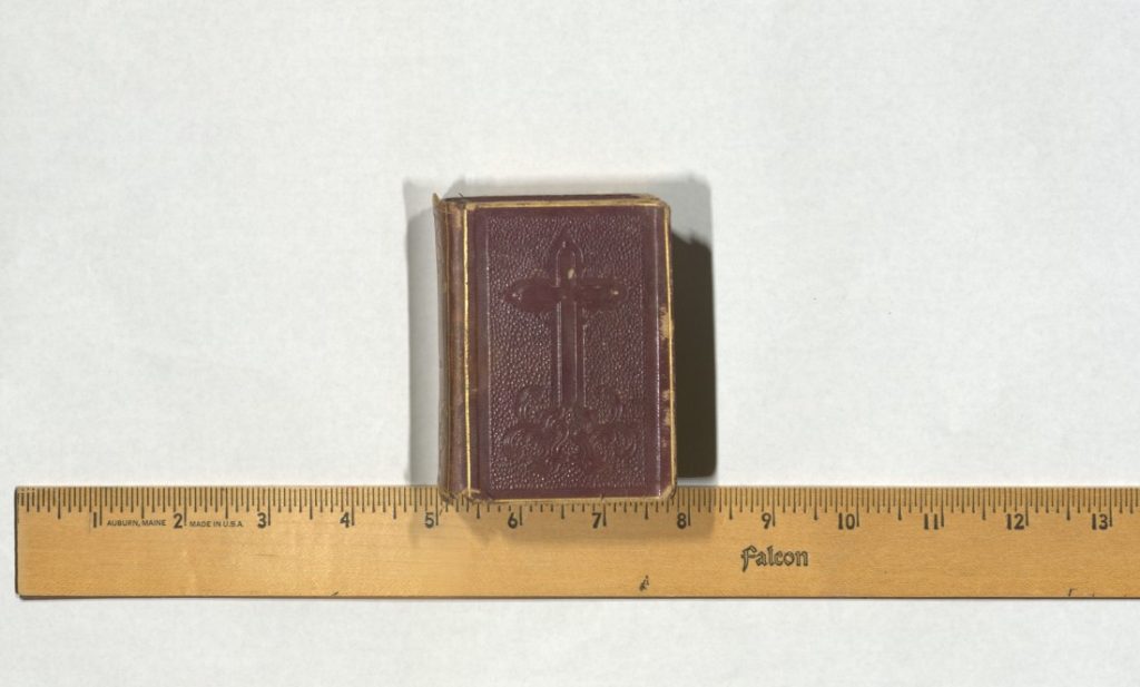 Book with a large embossed cross on the cover sitting above a ruler showing that the volume is almost three inches wide.