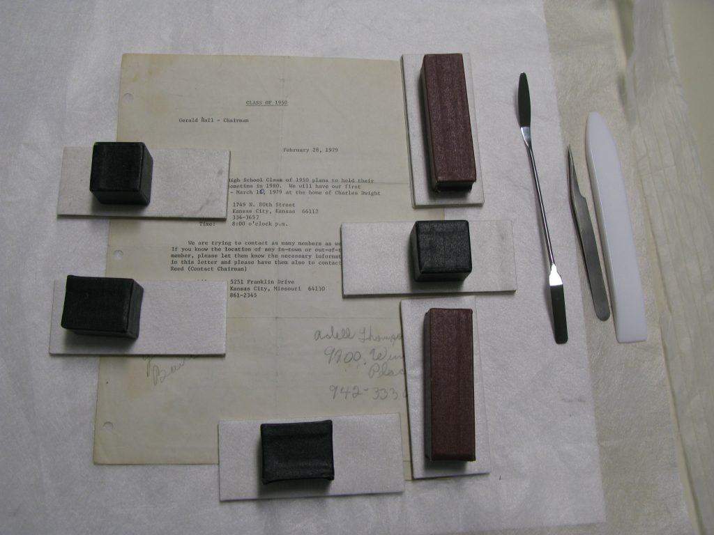 Typed piece of paper with weighted mending boards on top. Microspatula, tweezers, Teflon folder to the right of the paper.