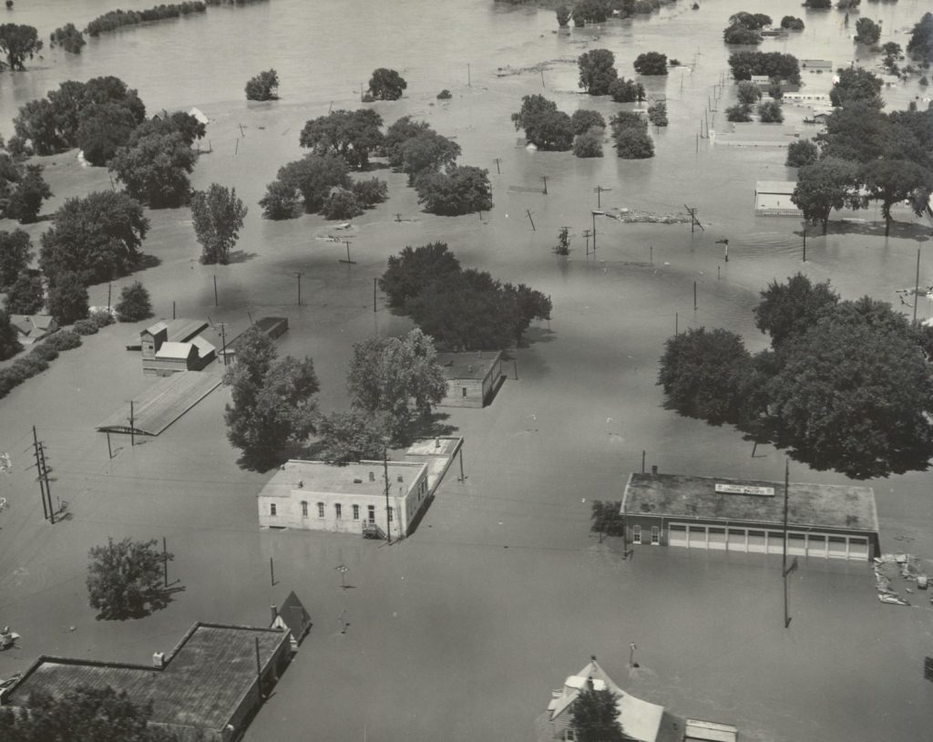 Black-and-white aerial photo of buildings and trees submerged in water.