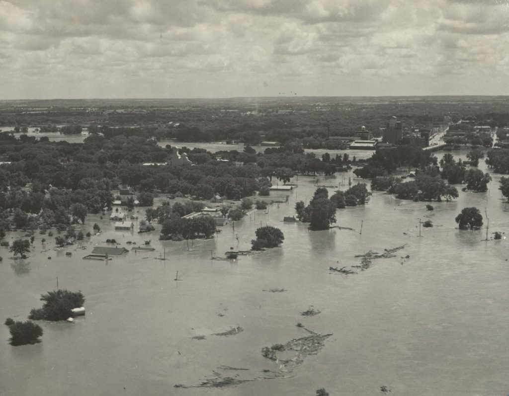 Black-and-white aerial photograph of buildings and trees submerged in water.
