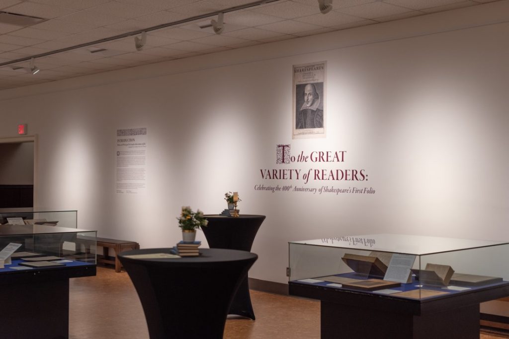 Three exhibit cases interspersed with two cocktail tables, with the exhibit title graphic in the background. 