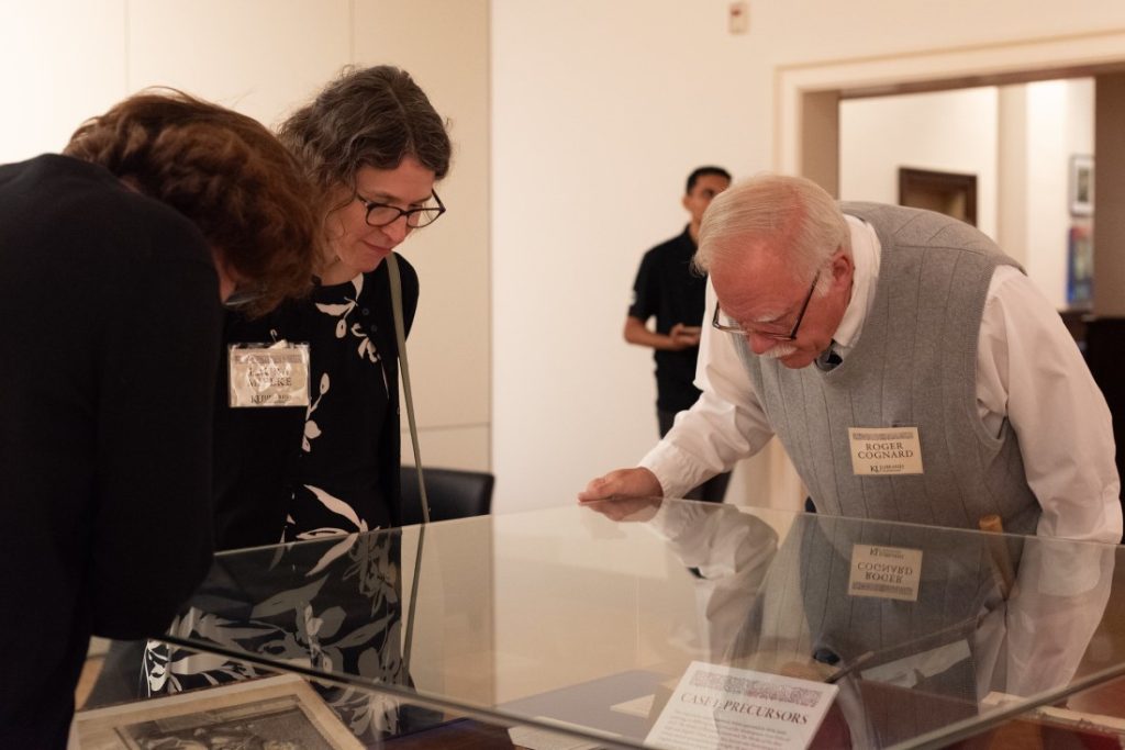 Three people looking down at items in an exhibit case.