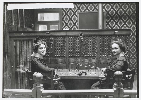 Black-and-white photograph of two young women sitting at a large switchboard.