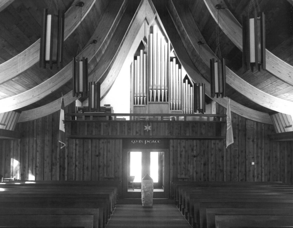 Black-and-white photograph of a pipe organ in a balcony at the back of the church's sanctuary.