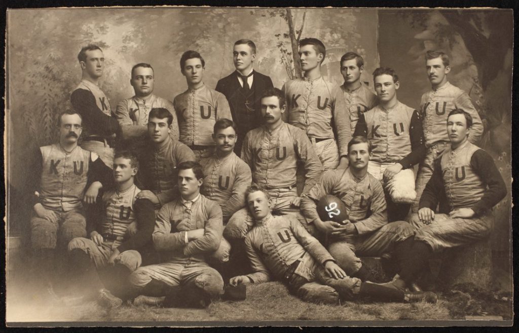 Black-and-white photograph of a group of young men; all are wearing light colored uniforms with "KU" on the front.