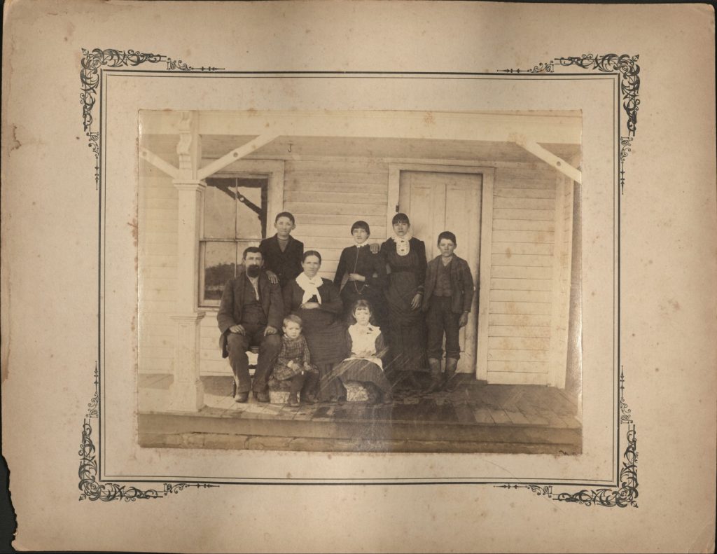 Sepia-toned photograph of eight people together on a porch.
