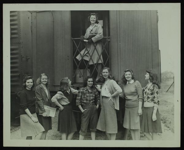 Black-and-white photograph of women standing next to a train car. 