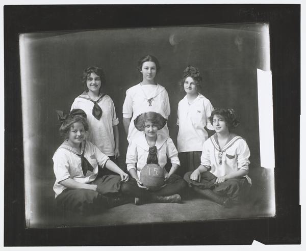 Black-and-white photograph of six girls in similar outfits. One girl is holding a basketball.