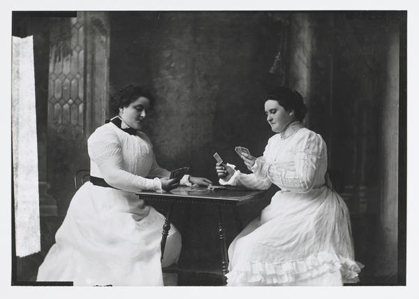 Black-and-white photograph of two women sitting at a small table, playing cards.