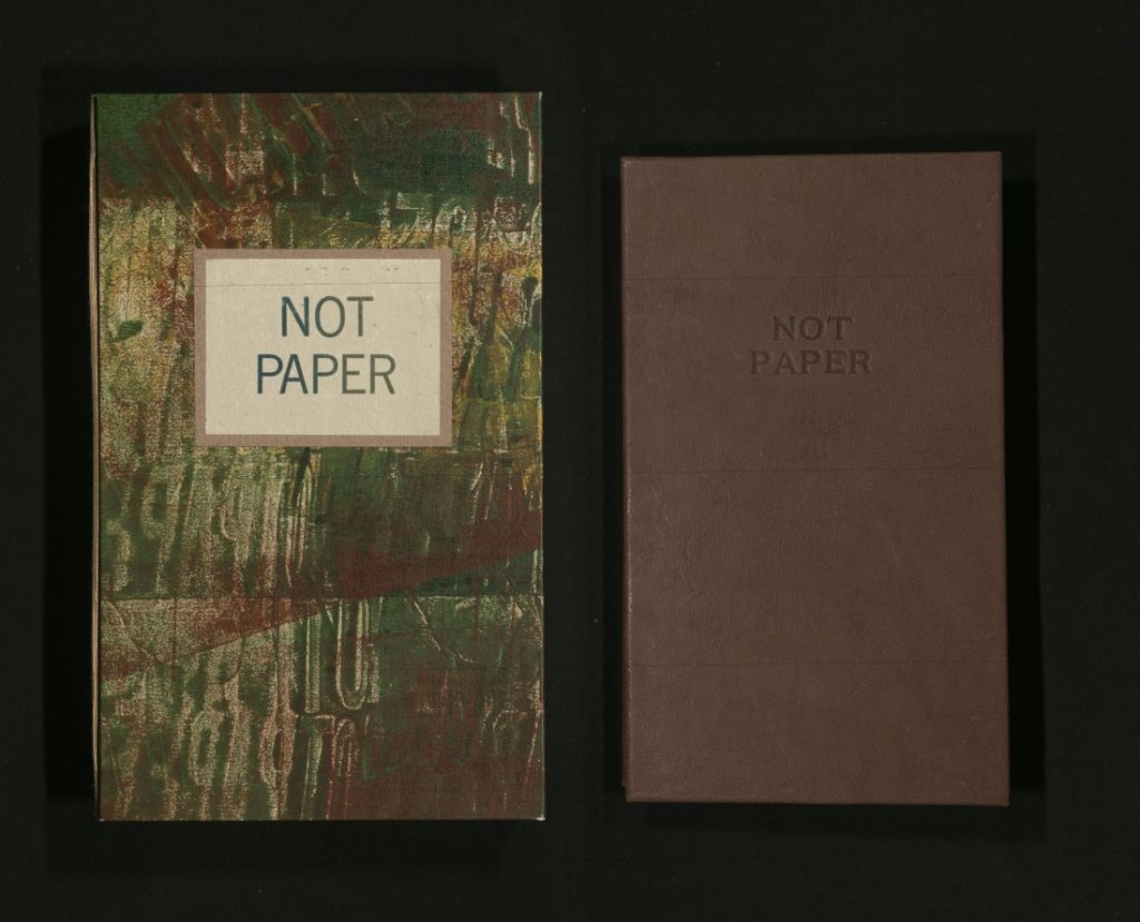 Two objects against a black background: on the left a book with the title against a marbled background and on the right a dark brown enclosure with an embossed title.