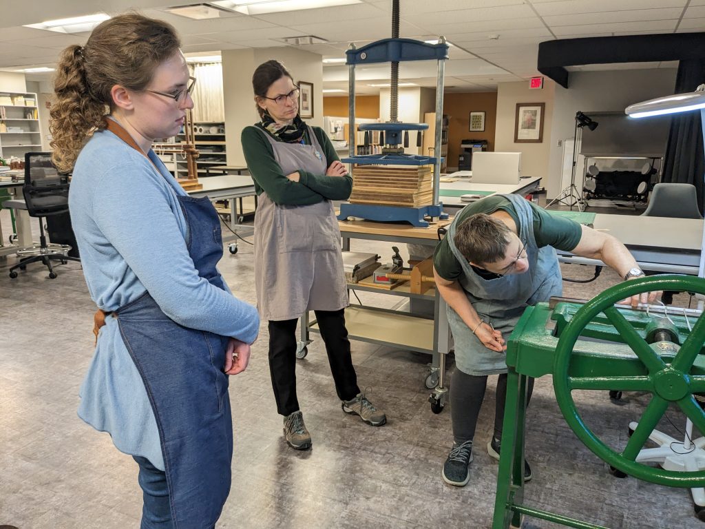 Conservators watch as Karen Hanmer demonstrates backing - shaping the spine of a book - on a job backer.