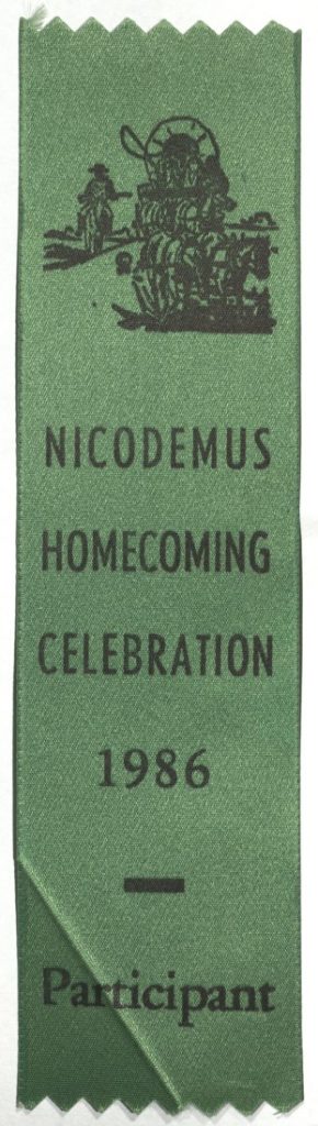 Black ink sketch of people in a covered wagon pulled by horses with the text "Nicodemus Homecoming Celebration 1986 Participant," all against a green background.