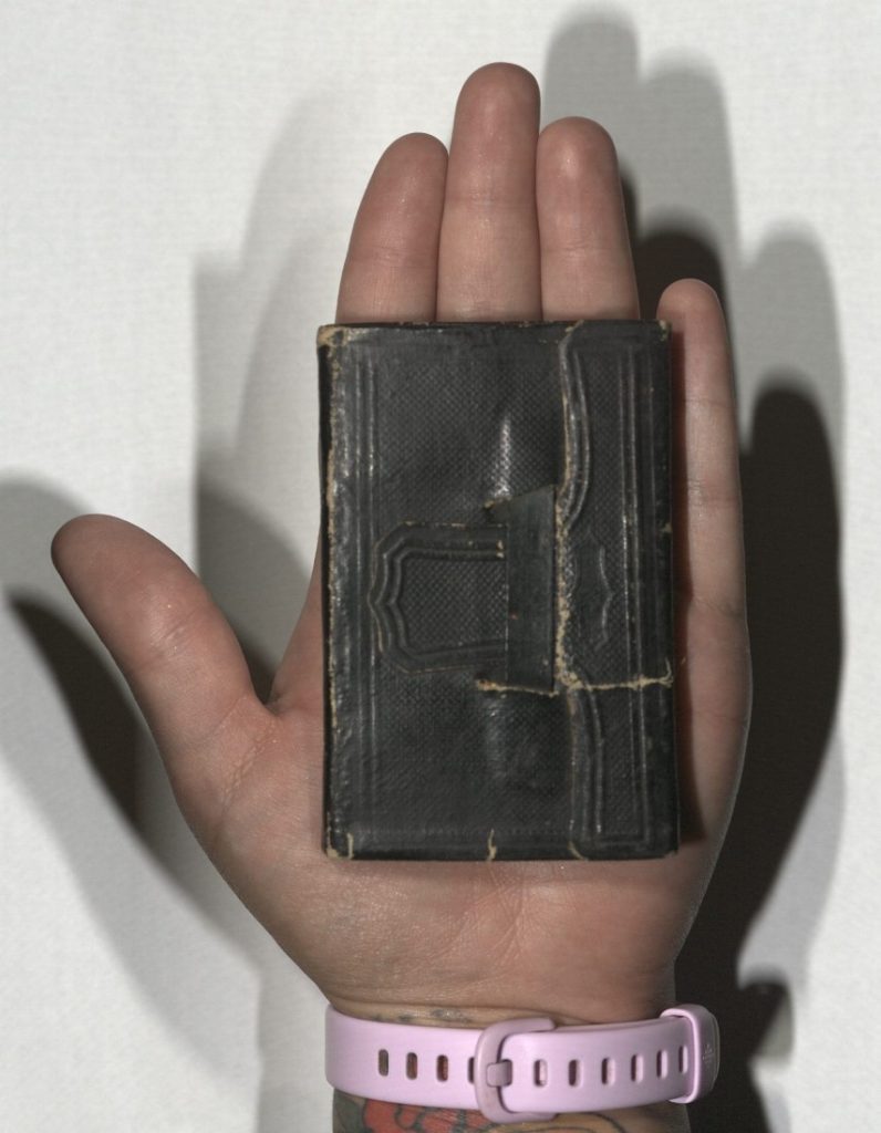 Small volume enclosed in a brown leather cover, sitting in someone's hand to show the book's small size.