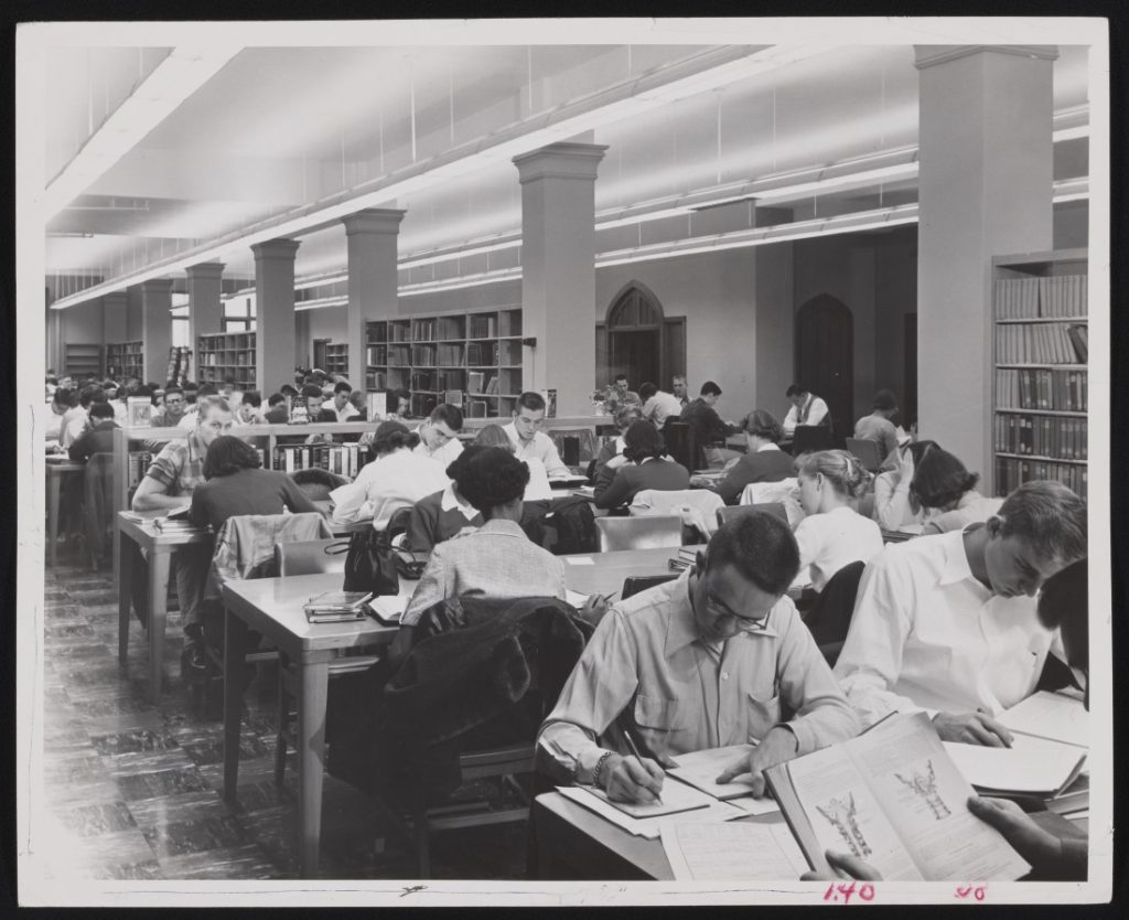 Black-and-white photograph of students sitting and reading at long tables. 