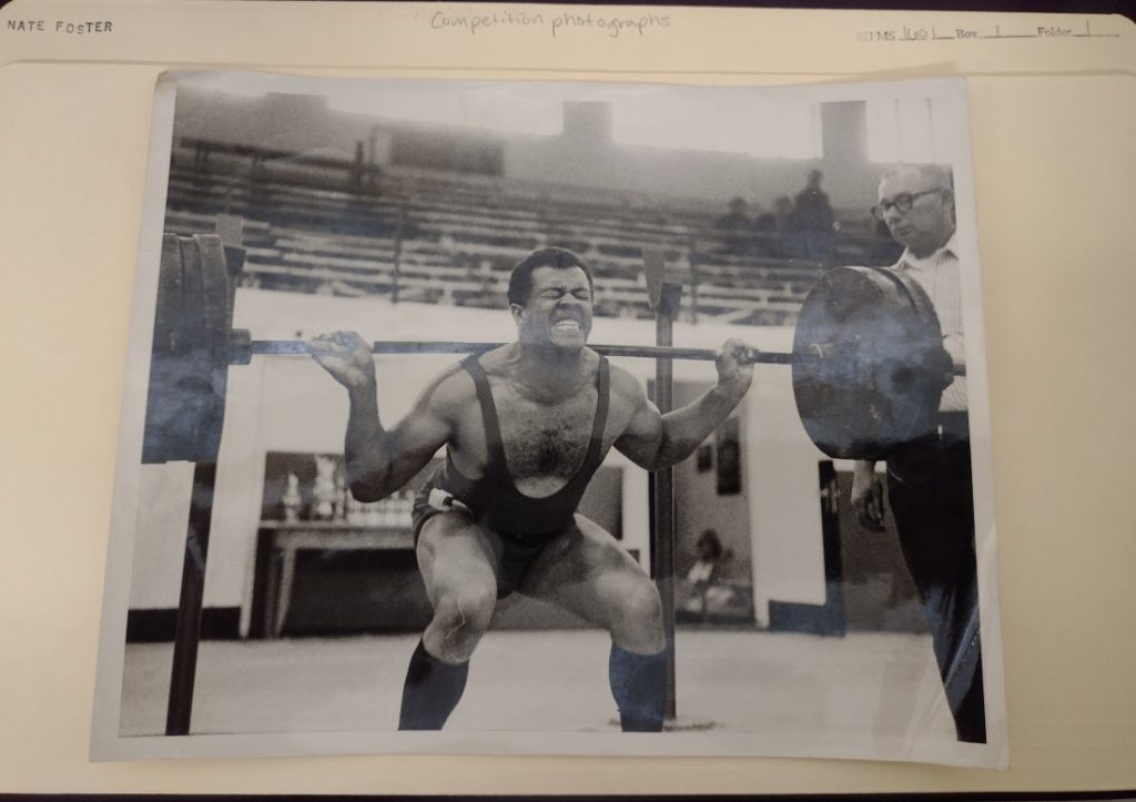 Black-and-white photograph of a man lifting a large barbell weight.