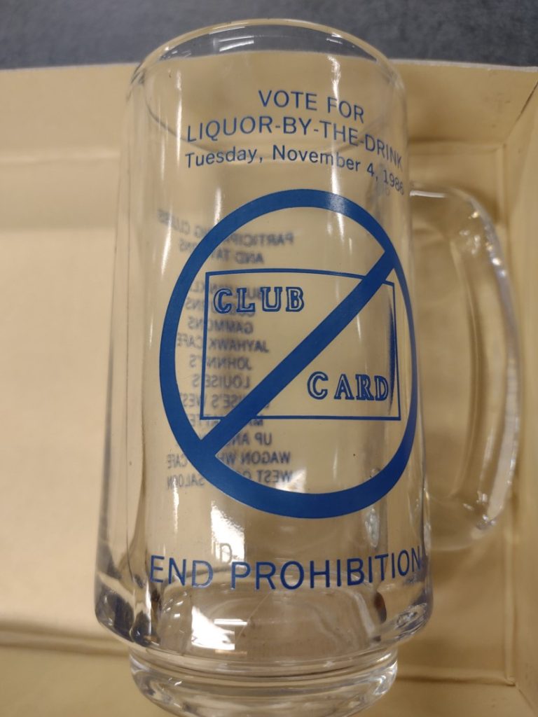 Photograph of a clear glass beer mug that has text in blue.