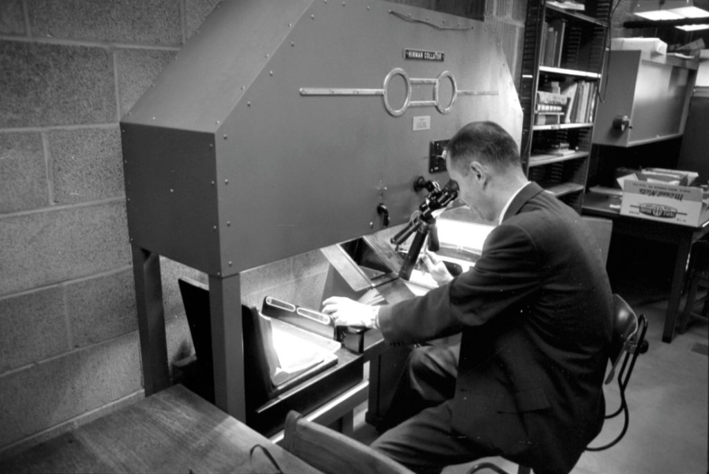 Black-and-white photograph sitting in front of a large piece of equipment and looking through an eyepiece.