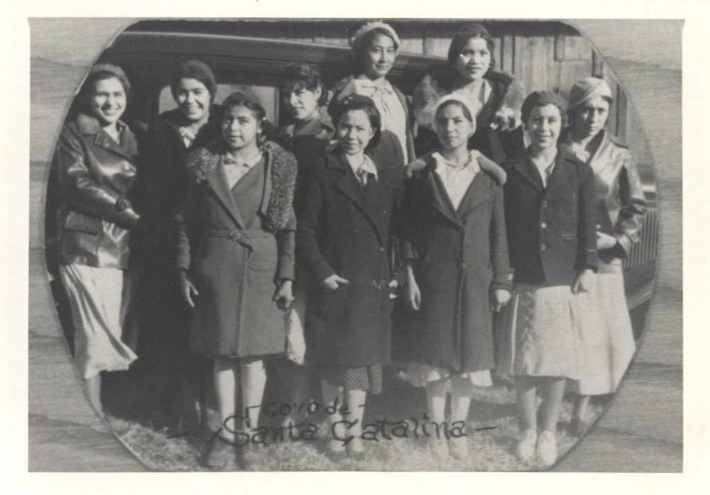 Black-and-white photo of a group of young women standing in front of a car.