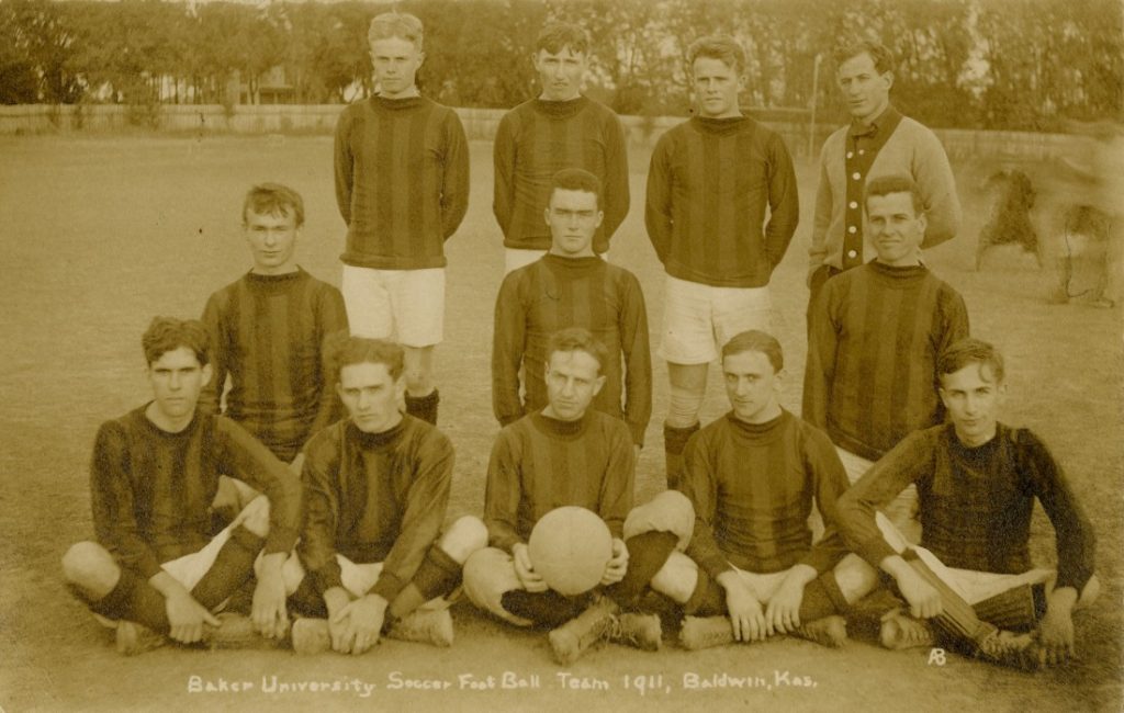 Sepia-toned photograph of a group of young men in white shorts, striped long-sleeve shirts, and dark knee-high socks.