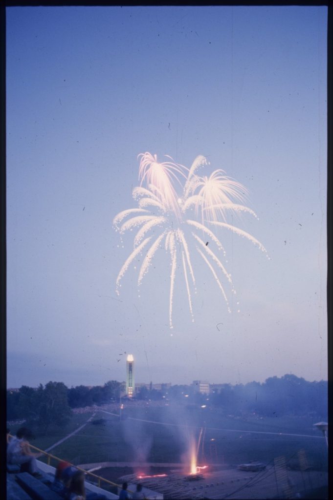 Color photograph of fireworks exploding above KU's Campanile and Memorial Stadium.