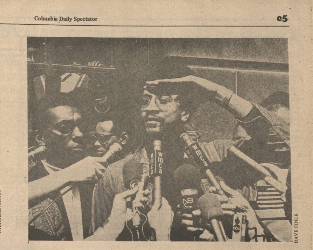 Black-and-white photograph of two Black men with numerous microphones held by reporters.