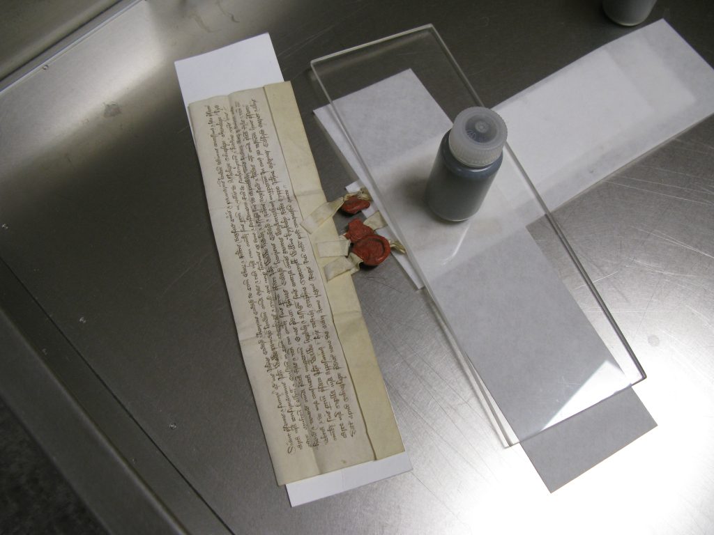 Part of a parchment document is humidified with damp blotter, under light weight.